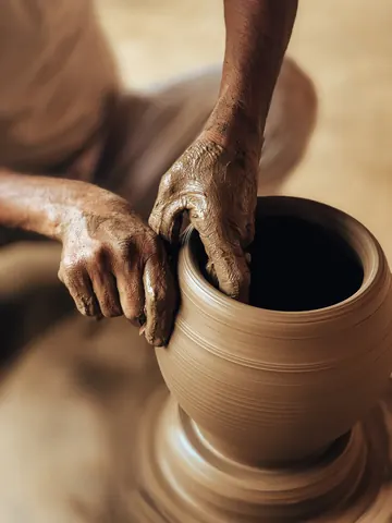 Steady hands guide the rim of a turning pot.