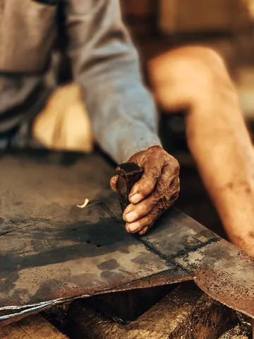 A craftsman's hand rests on a worn blade.