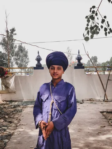 A young figure in blue stands in a sunlit courtyard.