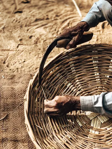 Hands and a curved blade work along a basket's rim.