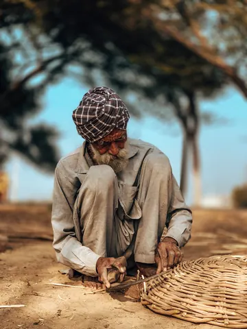 A basket weaver works on the ground beneath the trees.