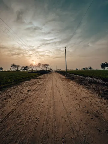 A quiet dirt road leads towards the evening sky.