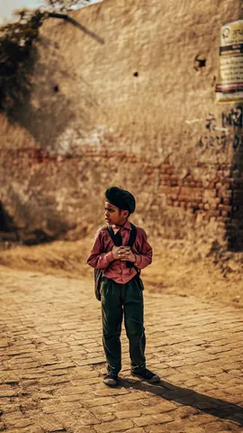 A child stands against the warm tones of an old wall.
