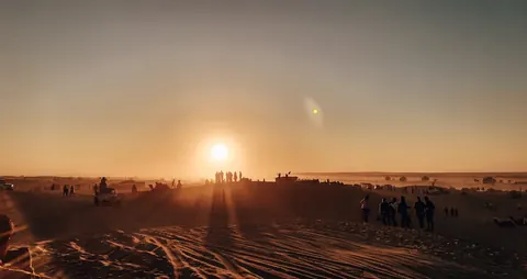 The setting sun lights a gathering on the dunes.