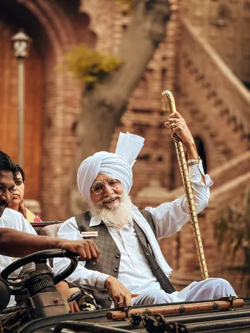 A smiling elder lifts his walking stick from an open vehicle.