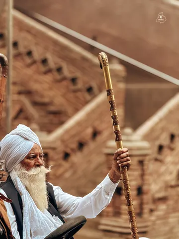 Hands hold a carved walking stick against a brick backdrop.