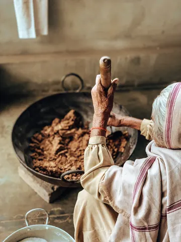 An elder works beside a broad cooking pan.