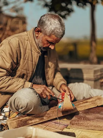 A shoemaker works at a low bench in the open air.