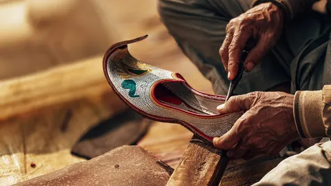 Careful hands shape an embroidered shoe.