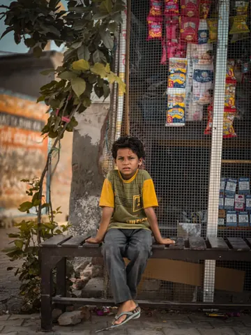 A child rests on a bench outside a small shop.